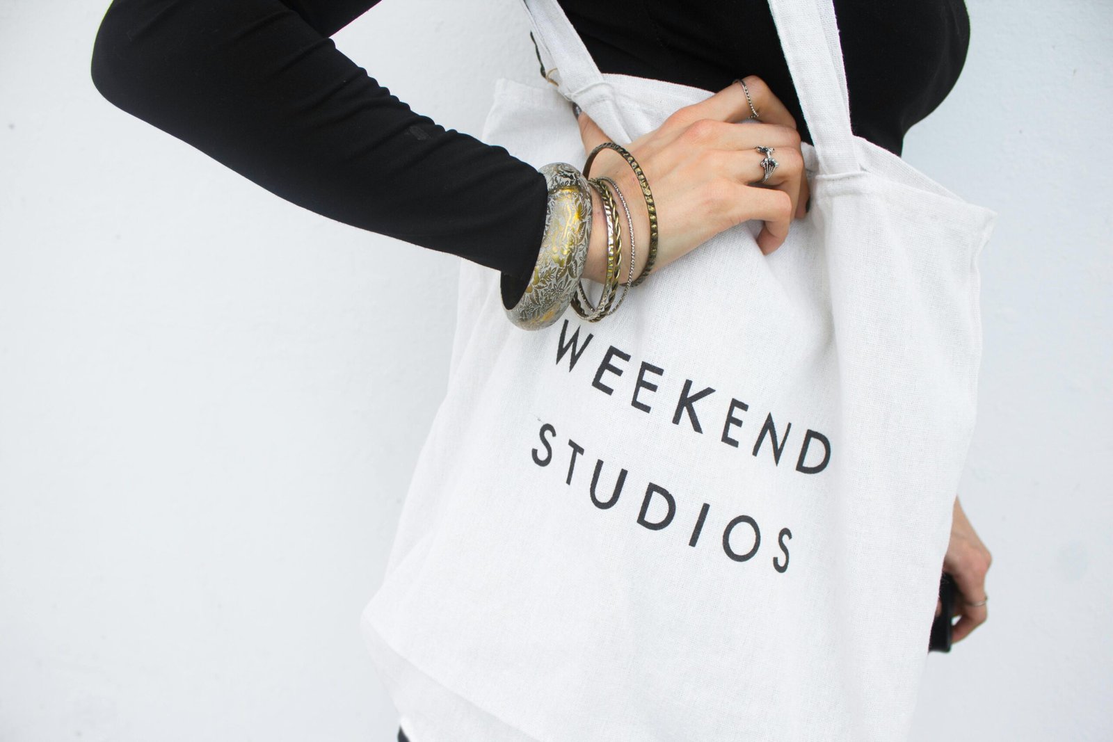 Stylish tote bag with 'Weekend Studios' text, worn casually with elegant bracelets.